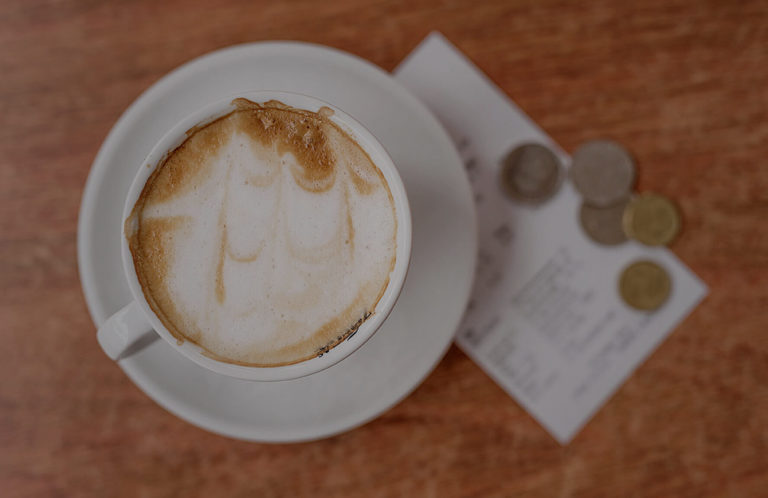 Cappuccino på fat bredvid kvitto och mynt